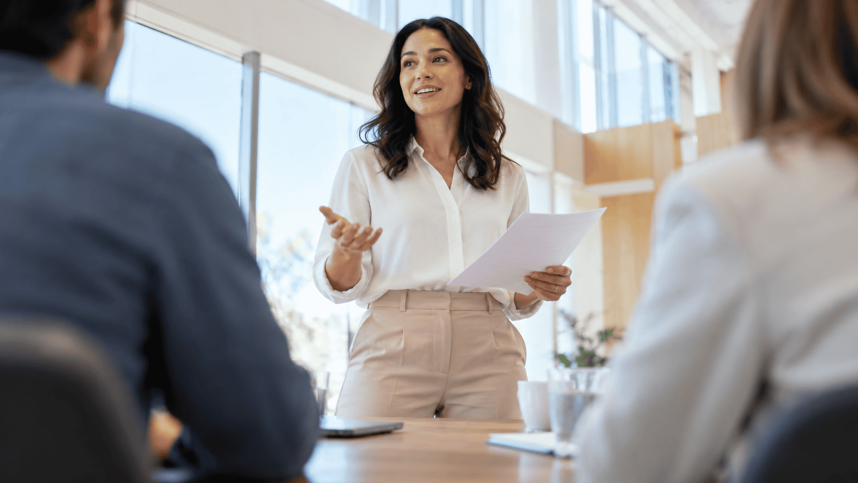 Manager standing at the head of a table asking the group a direct question, a core skill in how to run effective meetings